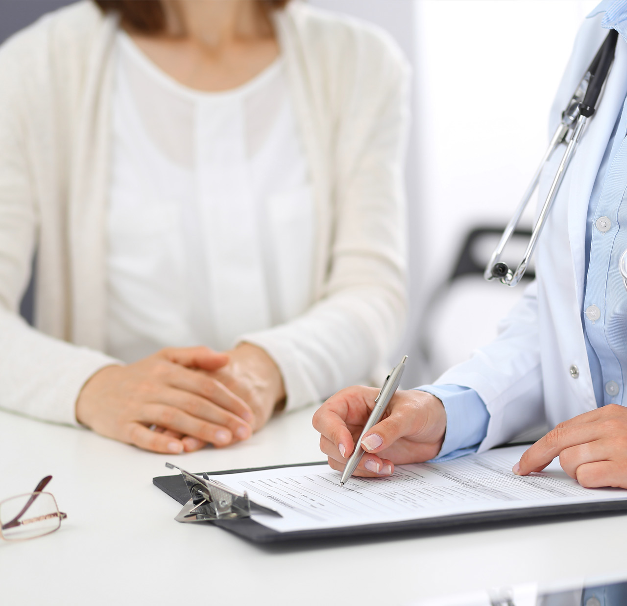 Unknown doctor and female patient discussing something while standing near reception desk in emergency hospital. Physician at work in clinic. Medicine and health care concept